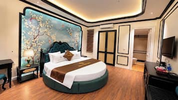 A modern hotel room with a round bed, a large wall mural, a flat-screen TV, and a wooden floor.