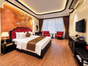 Habitación de hotel con una cama grande, un escritorio, dos sillas, un televisor y un minibar.