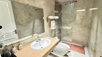 A bathroom with a marble sink, a toilet, and a glass-enclosed shower.
