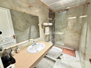 Un baño con lavamanos de mármol, inodoro y ducha con cerramiento de vidrio.