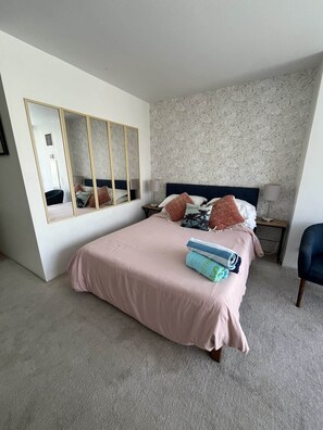 A bedroom with a large mirror, a bed with pink bedding, a nightstand with a lamp, and a chair. - Ilikai Marina condo for rent with free parking (Honolulu)