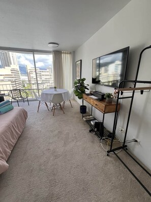 A modern bedroom with a large window, a bed, a desk with a TV, and a balcony. - Ilikai Marina condo for rent with free parking (Honolulu)