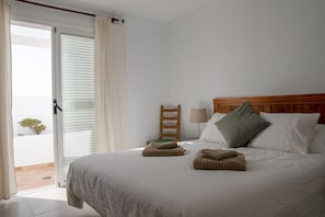 Ein Hotelzimmer mit einem Bett, einem hölzernen Kopfteil, einem Nachttisch, einer Lampe und Blick ins Freie.