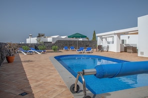 A swimming pool with blue tiles, surrounded by lounge chairs and a stone wall. - Villa Coloradas | large Sunny Terrace & Pool | Private Paradise (Playa Blanca)