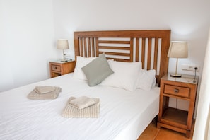 A neatly made bed with a wooden headboard, two bedside tables with lamps, and towels on the bed. - Villa Coloradas | large Sunny Terrace & Pool | Private Paradise (Playa Blanca)