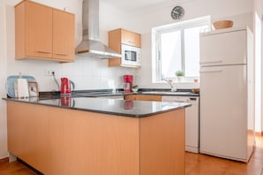 Eine moderne Küche mit Holzausstattung, einer Mittelinsel, einem Backofen, einer Mikrowelle, einem Geschirrspüler und einem Kühlschrank.