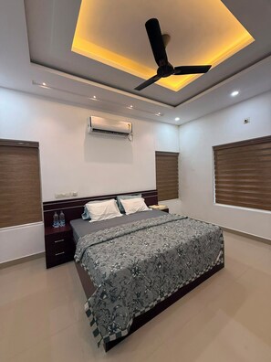 Une chambre moderne avec un lit placé au centre, un ventilateur de plafond et un appareil de climatisation.