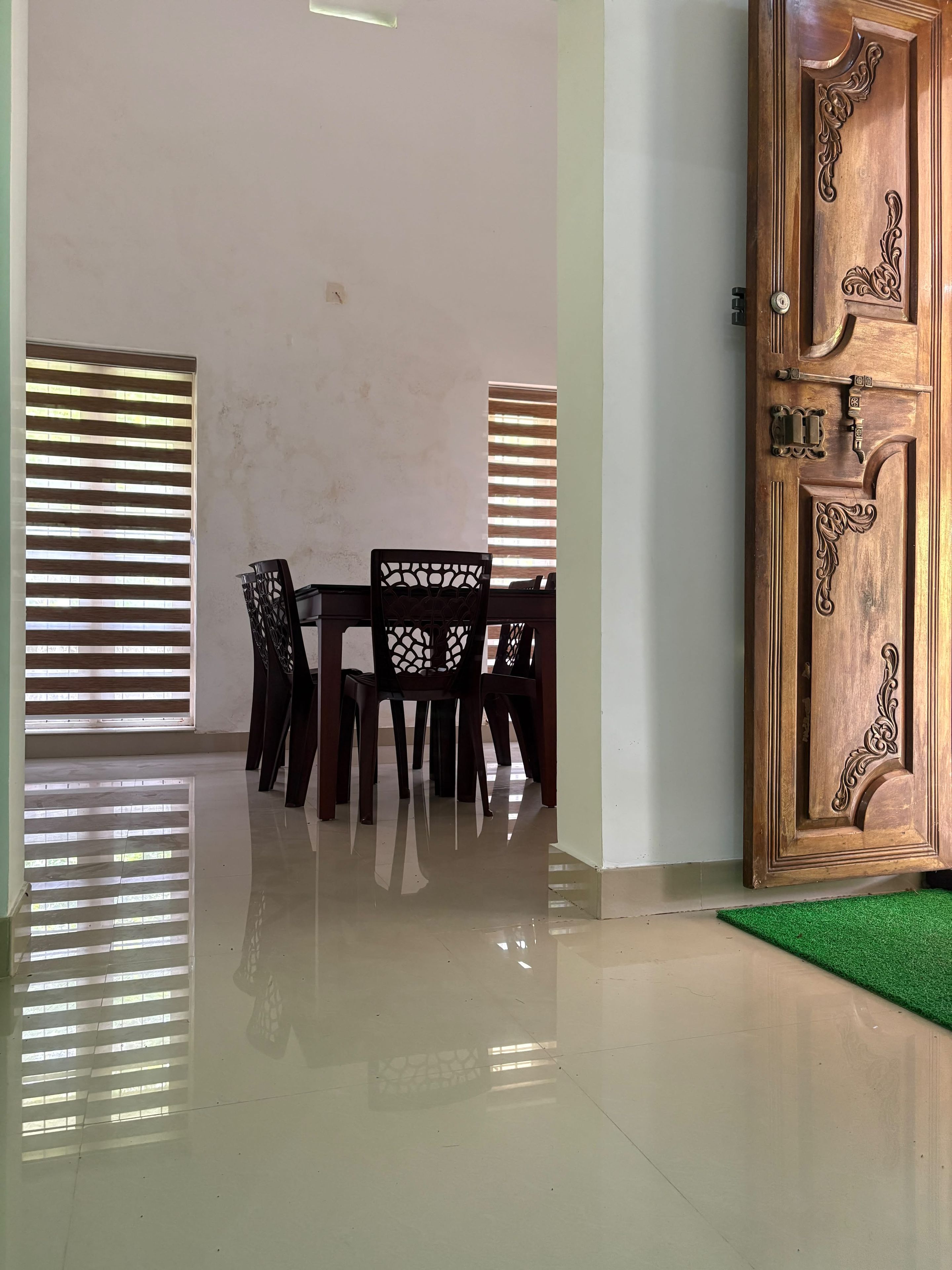 A room with a wooden door, a dining table with chairs, and a green mat.