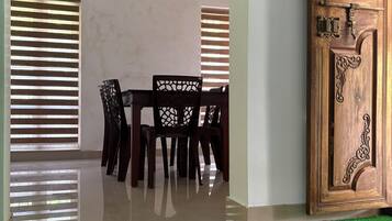 A room with a wooden door, a dining table with chairs, and a green mat.