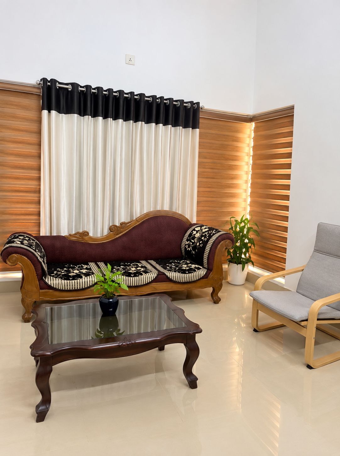 A room with a wooden sofa, a grey armchair, a glass coffee table, and a potted plant.