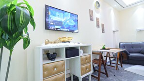 A modern living room with a flat-screen TV, a sofa, a dining table with chairs, and decorative items on the walls. - Modern Studio With SeaView  Pool & Gym (Ajman)