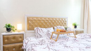 Un lit bien fait, recouvert d’une couvre-lit à motifs floraux, une table de chevet avec une lampe et un plateau contenant des éléments pour le petit-déjeuner.