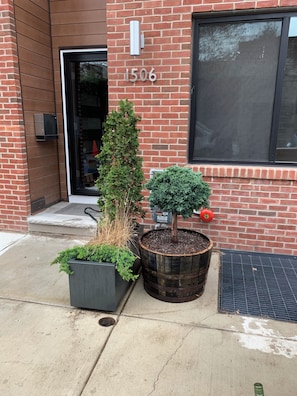 A brick building with a door and window, a mailbox, and potted plants. - Serene 3-bedroom house with parking for relaxing stays (Unknown)