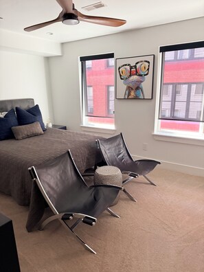 A bedroom with a bed, two chairs, a ceiling fan, and two windows with artwork. - Serene 3-bedroom house with parking for relaxing stays (Unknown)