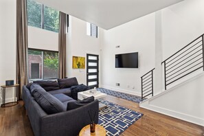 A modern living room with a grey sofa, a coffee table, and a TV mounted on the wall. - Serene 3-bedroom house with parking for relaxing stays (Unknown)