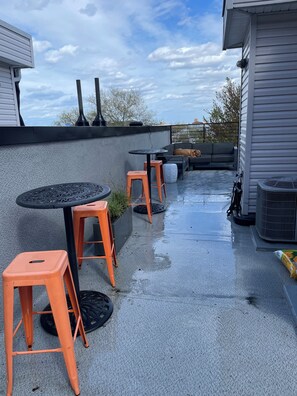 An outdoor patio area with a round table and orange stools, a grey sofa, and a black grill. - Serene 3-bedroom house with parking for relaxing stays (Unknown)