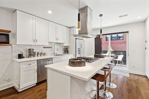 A modern kitchen with white cabinetry, stainless steel appliances, and a central island with stools. - Serene 3-bedroom house with parking for relaxing stays (Unknown)