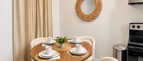 Un coin repas comprenant une table ronde, quatre chaises, un luminaire suspendu, un miroir fixé au mur et une cuisinière.