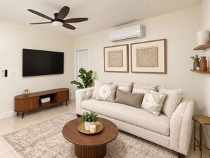 A living room with a sofa, a coffee table, a TV, a ceiling fan, and framed artwork on the wall. - Aqua Suites (Nassau)