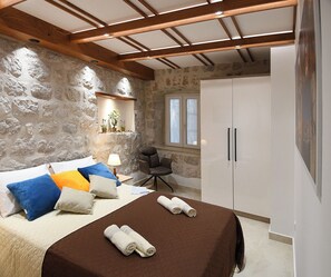 Ein Schlafzimmer mit einem Bett, Kissen, einem Sessel, einem Kleiderschrank und einer Steinwand.