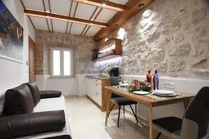 A compact kitchen with a stone wall, wooden ceiling beams, and a dining area with a table set for two. - Perfect 1-bedroom apartment with ACin Dubrovnik,quiet Street, steps from Stradun (Dubrovnik)
