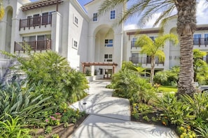 A multi-story building with a central courtyard, surrounded by lush greenery and palm trees. - Living the Resort Life - Pool (Carlsbad)