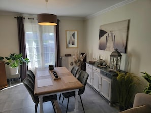 A dining area with a wooden table, chairs, a pendant light, and a cabinet with decorative items. - Cozy Vacation Rental - Porte de Chambord - Garden - Pets Allowed (Huisseau-sur-Cosson)