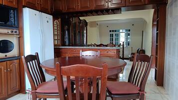 A dining area with a wooden table and chairs, a built-in oven, and a kitchen with wooden cabinets and a refrigerator.