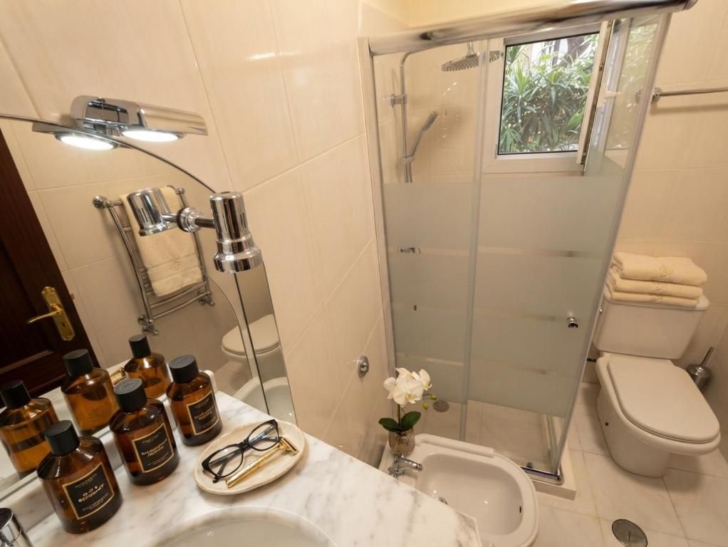 Uma casa de banho moderna com chuveiro em cabine de vidro, um bidé e uma sanita. Há artigos de higiene pessoal no lavatório.