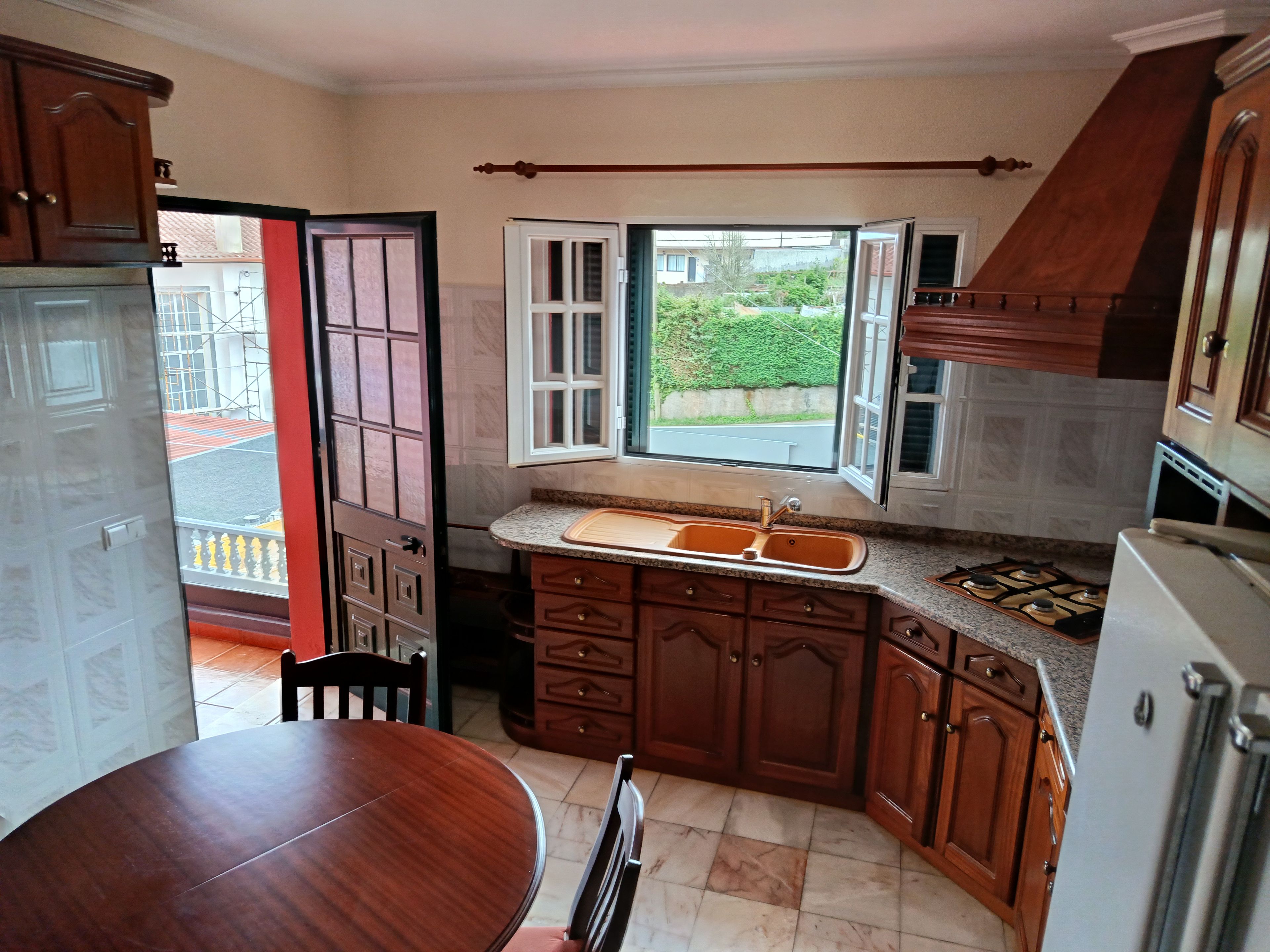 A kitchen with wooden cabinets, a gas stove, a sink, and a window providing a view of the outside.