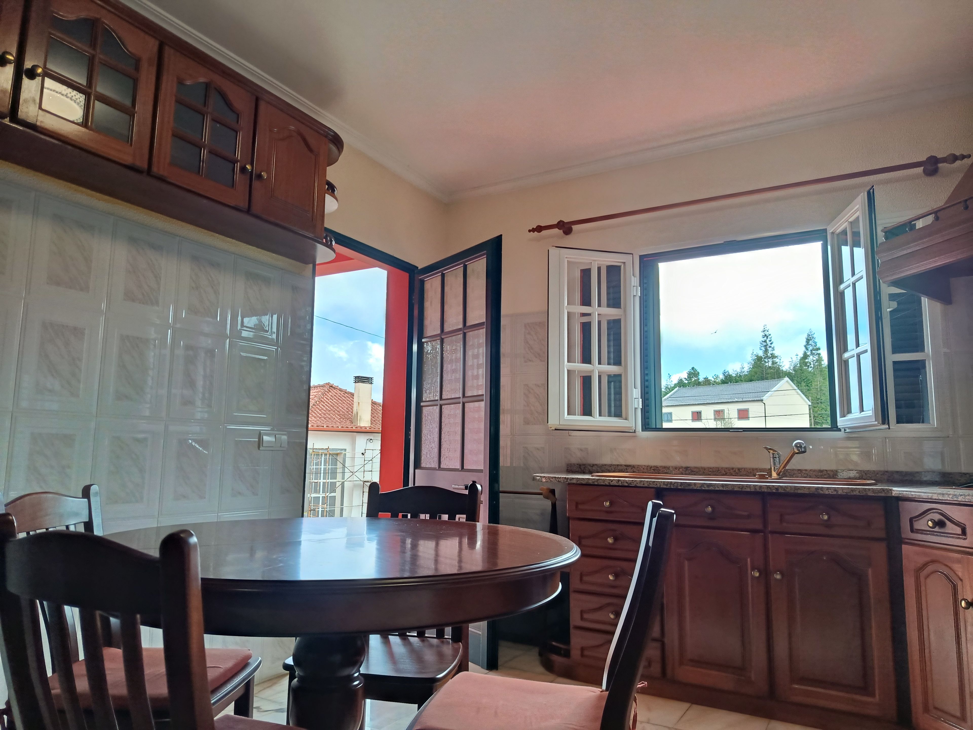 A kitchen with wooden cabinets, a dining table with chairs, and a window with a view of houses.