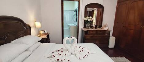 A hotel room with a bed, a nightstand with a lamp, a dresser, a mirror, and a wardrobe.