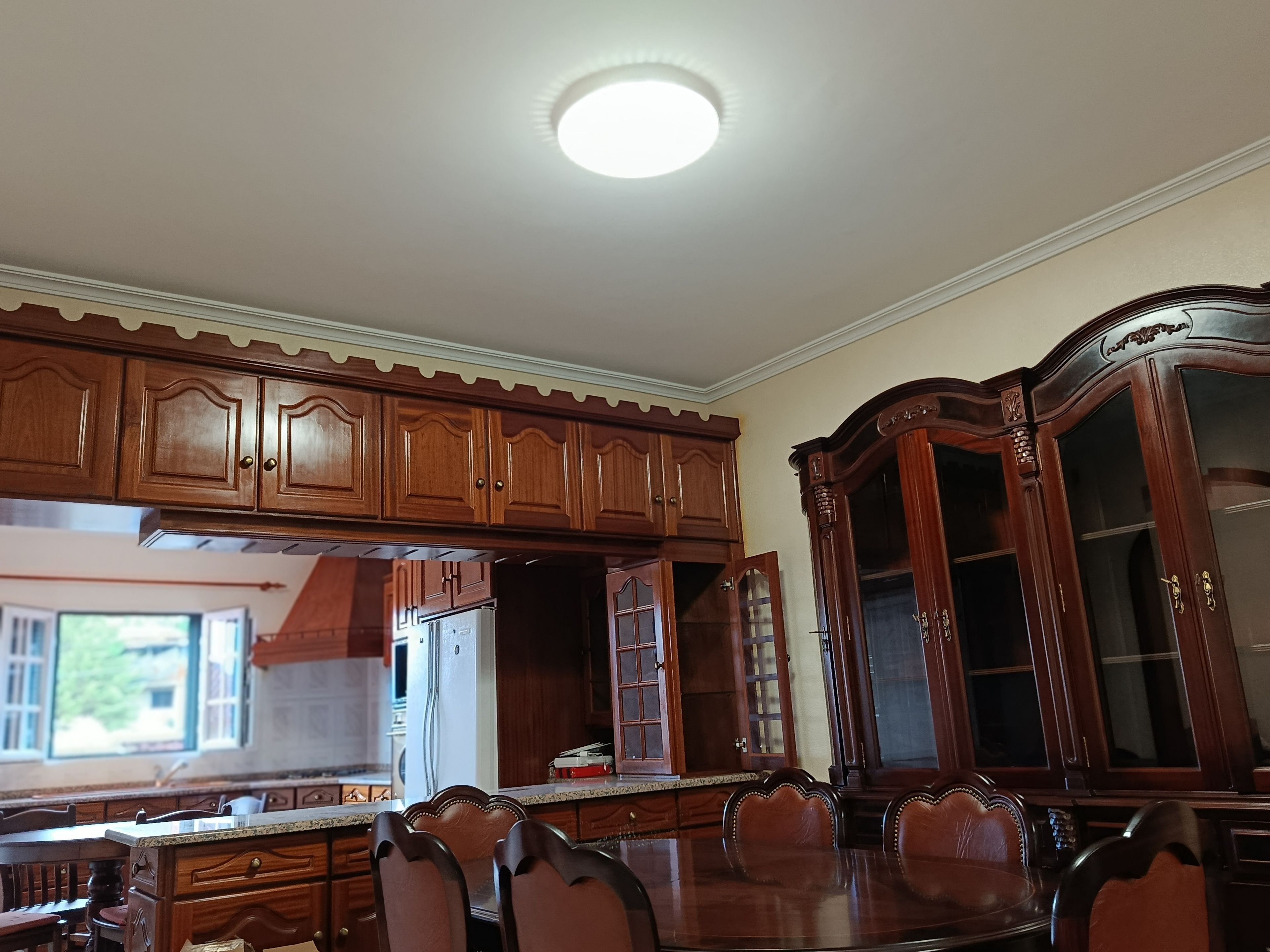 Cozinha com armários de madeira, mesa de jantar com cadeiras e forno embutido.