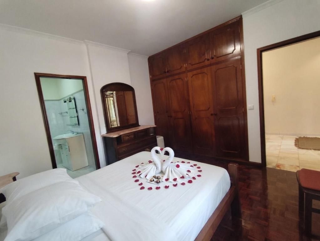 Une chambre d’hôtel avec un lit, une armoire en bois, un miroir et une salle de bain visible à travers une porte ouverte.