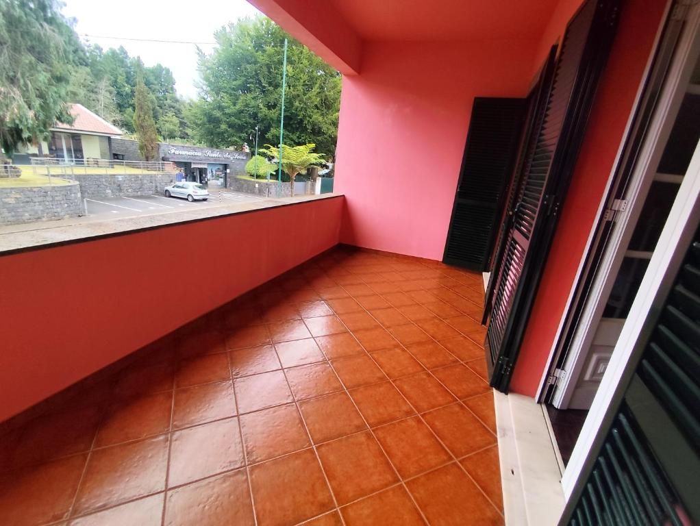A balcony with a tiled floor, a red wall, and a view of a building with a sign.