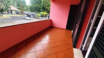 A balcony with a tiled floor, a red wall, and a view of a building with a sign.