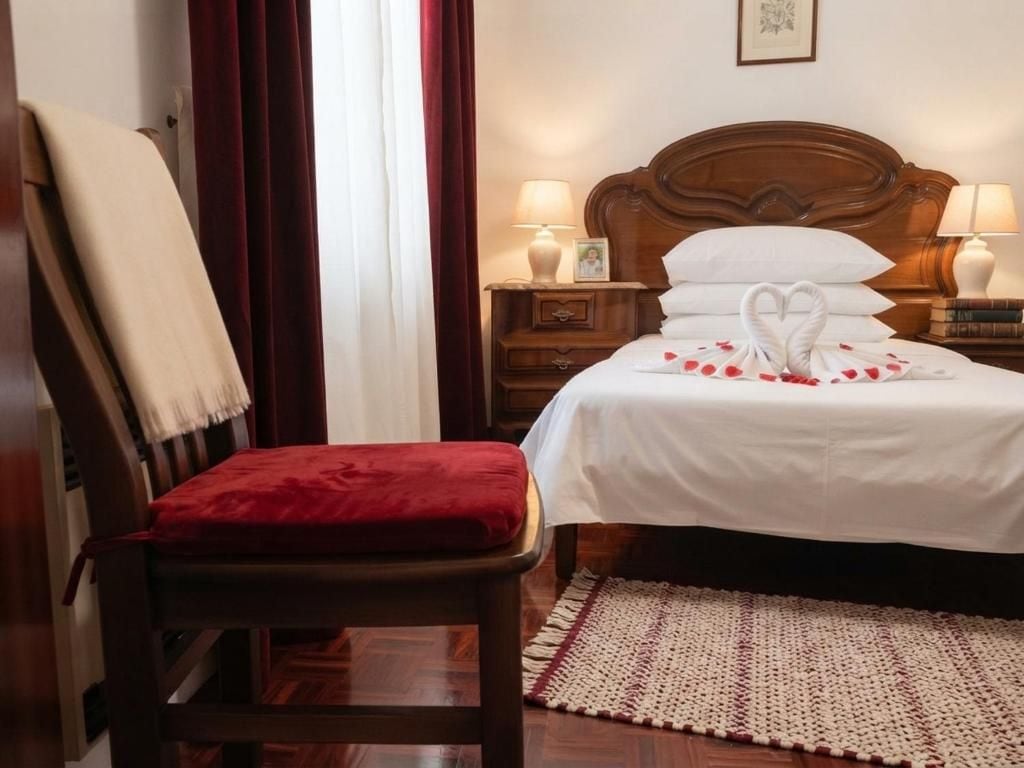 Una habitación de hotel con una cama de madera, una silla roja, una mesita de noche con una lámpara y una alfombra en el suelo.