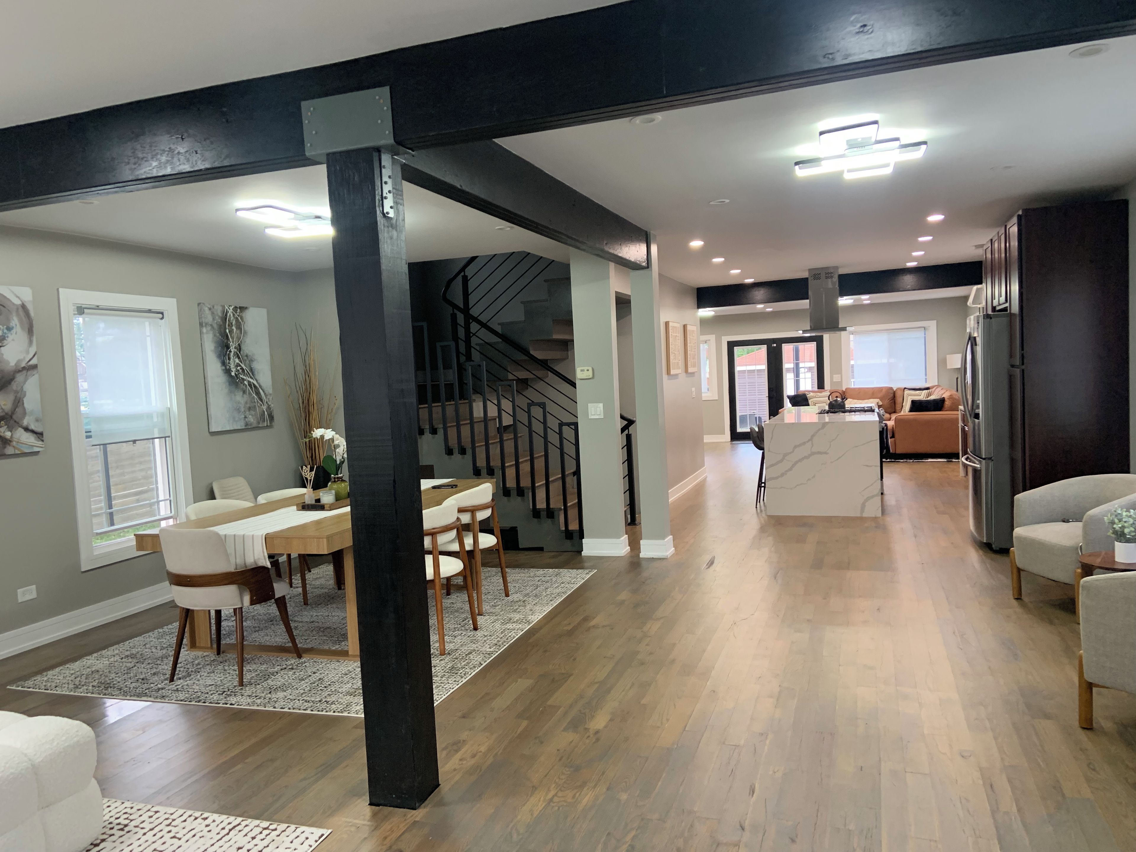 A spacious living area with a dining table, chairs, a kitchen island, and a staircase.