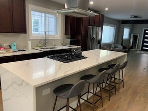 A modern kitchen with a central island, dark wood cabinets, stainless steel appliances, and a large window. - Oak and Onyx Spacious 4-bedroom house in wonderful Beverly Chicago with AC (Chicago)