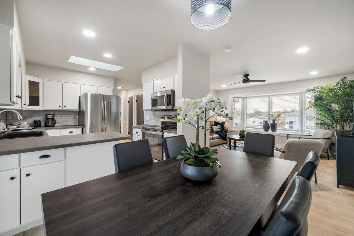 Une cuisine moderne avec des meubles blancs, des appareils en acier inoxydable et un coin repas comprenant une table et des chaises en bois foncé.