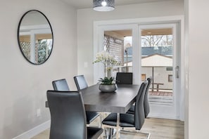 Een eethoek met een rechthoekige tafel, zes stoelen, een vaas met bloemen en een grote spiegel aan de muur.