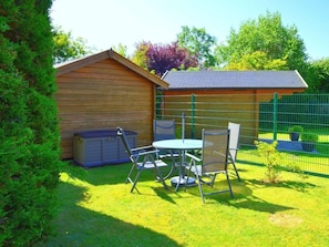 A wooden shed with a metal roof, a hot tub, and a table with chairs in a grassy yard. - Strandstrasse OG (Nieblum)