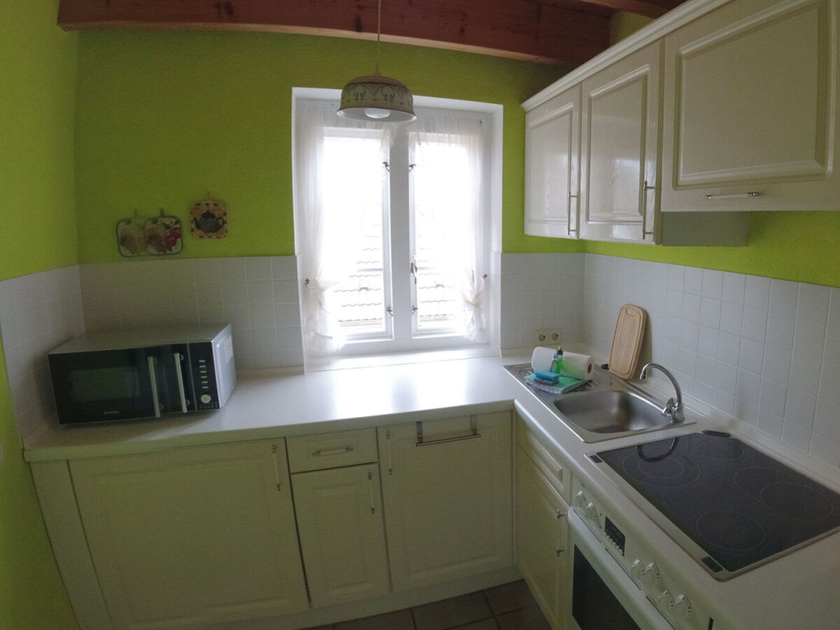 A kitchen with white cabinets, a microwave, a stove, and a window with curtains.