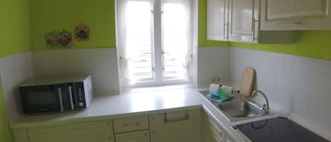 A kitchen with white cabinets, a microwave, a stove, and a window with curtains.