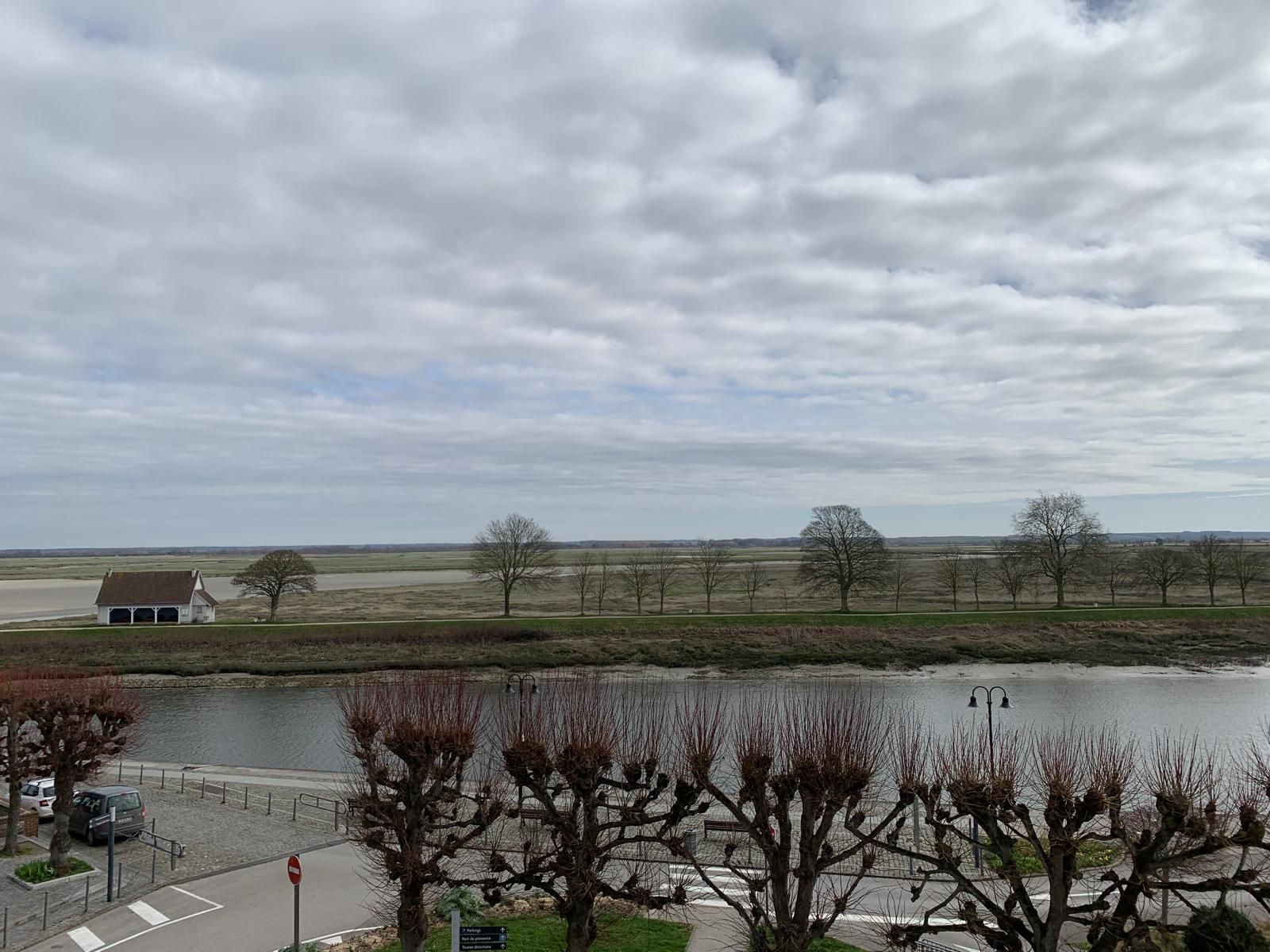 A view of a lakeside area with a building, trees, and a clear sky.