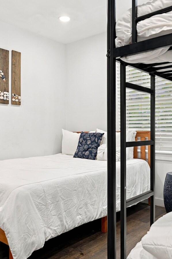 Een slaapkamer met een stapelbed, een wit bed, een blauw kussen en een houten hoofdbord.