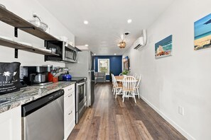 Een moderne keuken met een ingebouwde oven, magnetron en vaatwasser. Er is een eethoek met een houten tafel en witte stoelen.