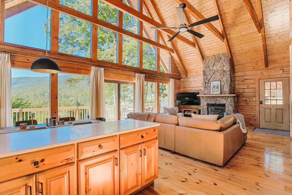A spacious living area with a stone fireplace, wooden ceiling beams, and large windows.