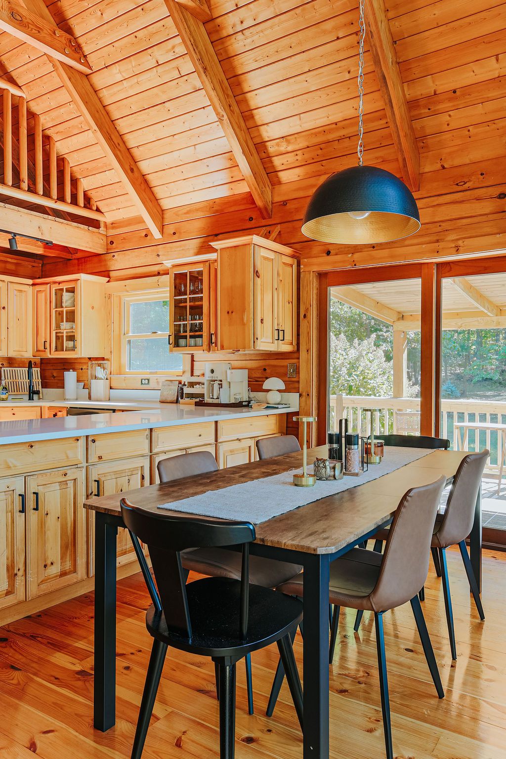 A spacious wooden cabin with a large dining table, multiple chairs, and a hanging pendant light.