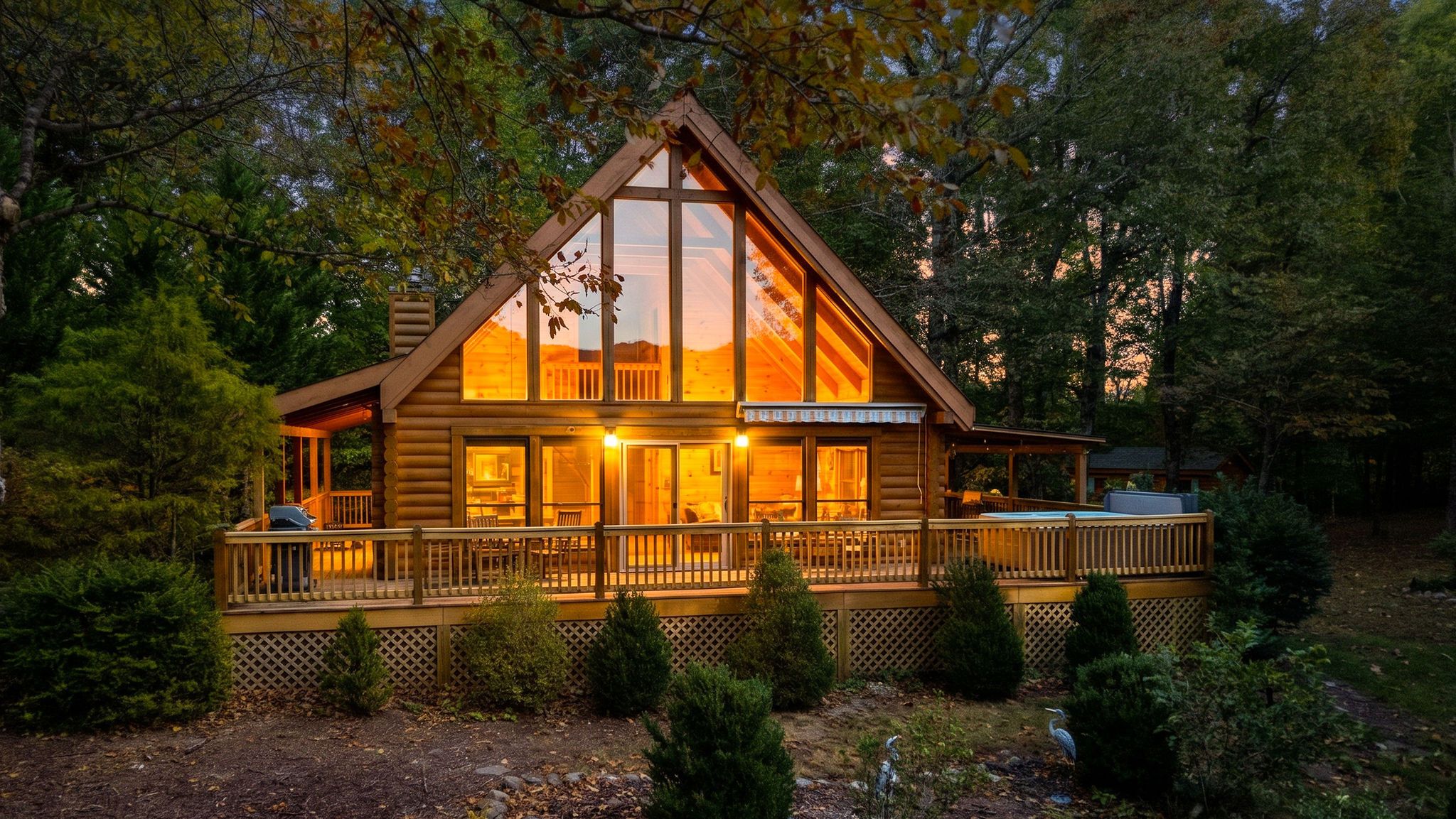 A log cabin with a large deck, surrounded by trees.